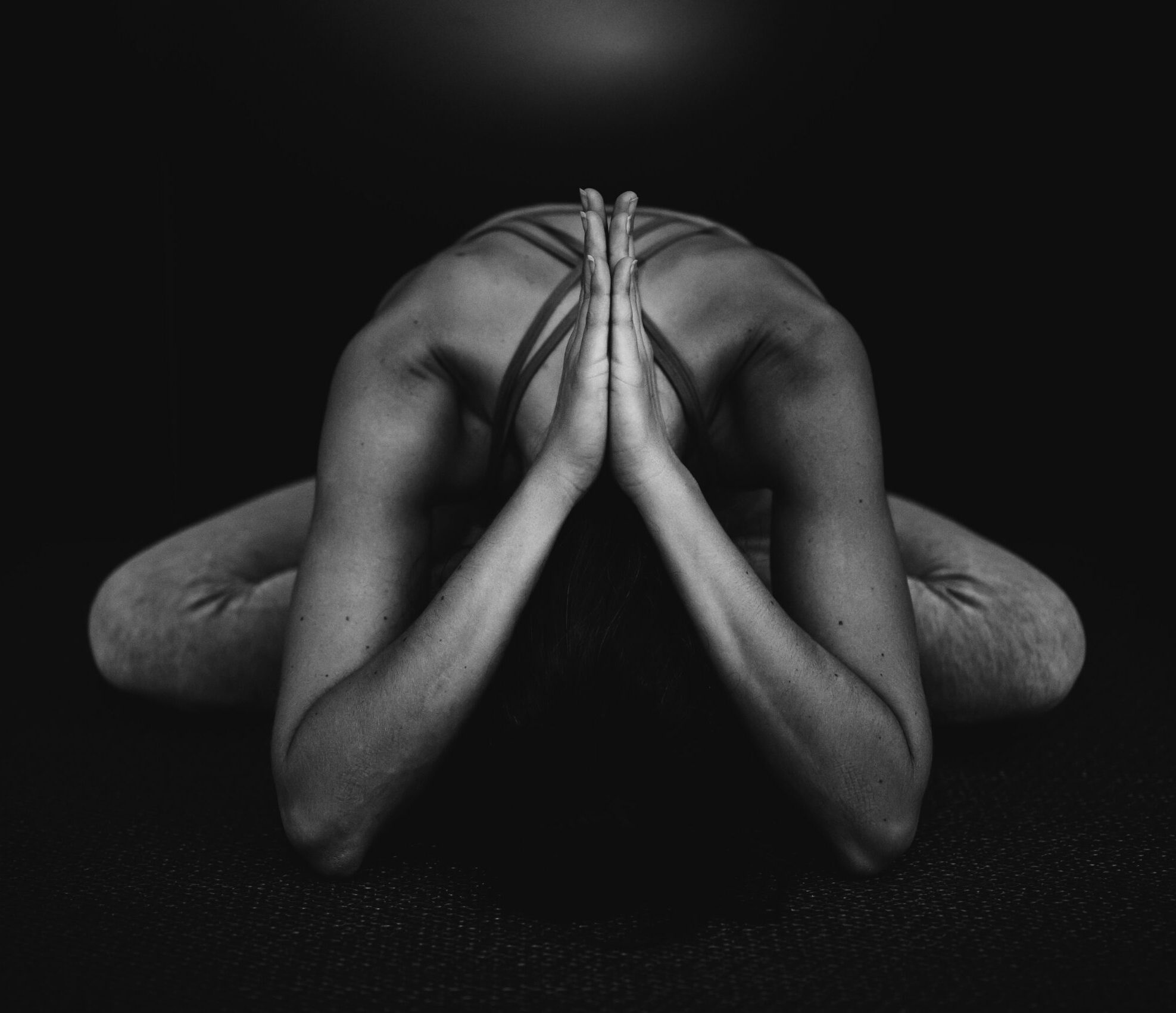 woman bending forward in sitting position with handpalms together over her neck.