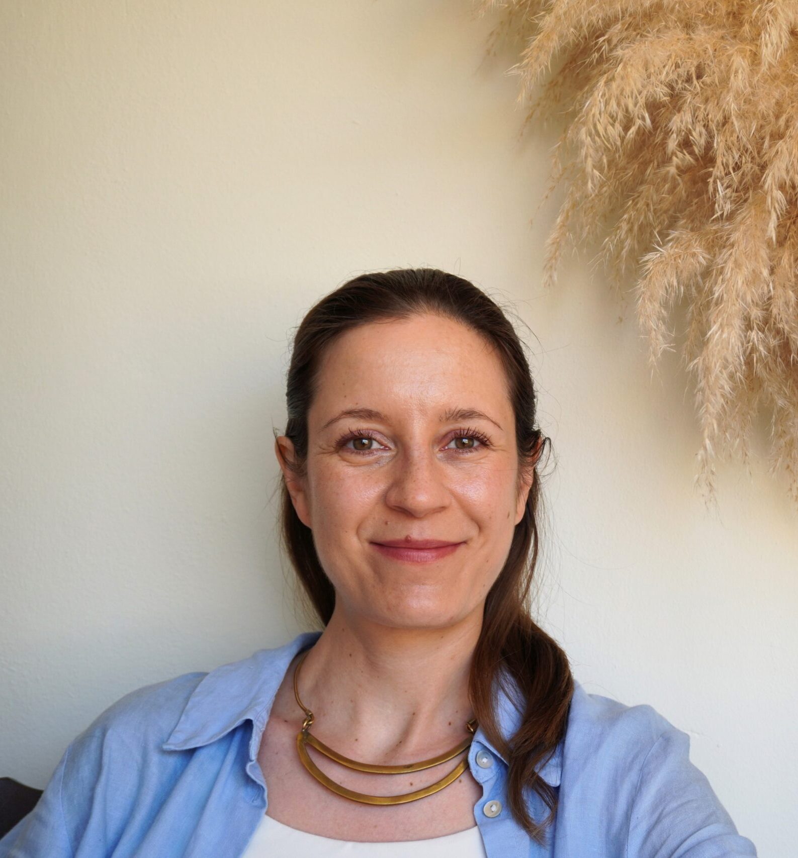 Woman with blue shirt and necklace gazing at the camera